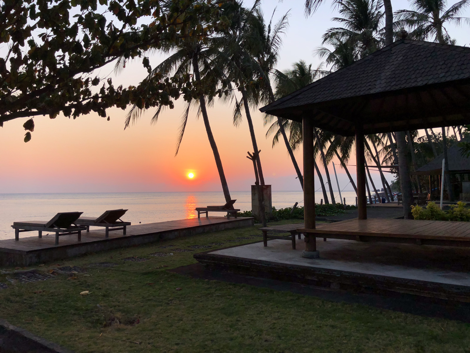 Sunrise over the Lombok Strait from the lawn, loungers set out on the terrace under a shingled pavilion.
