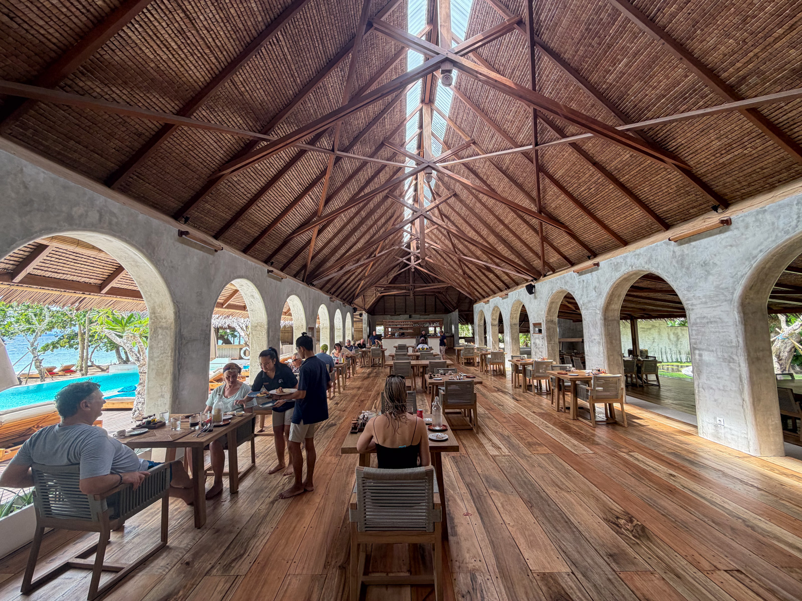 The dining hall under a high timber roof, arched openings down both sides and guests along the tables.