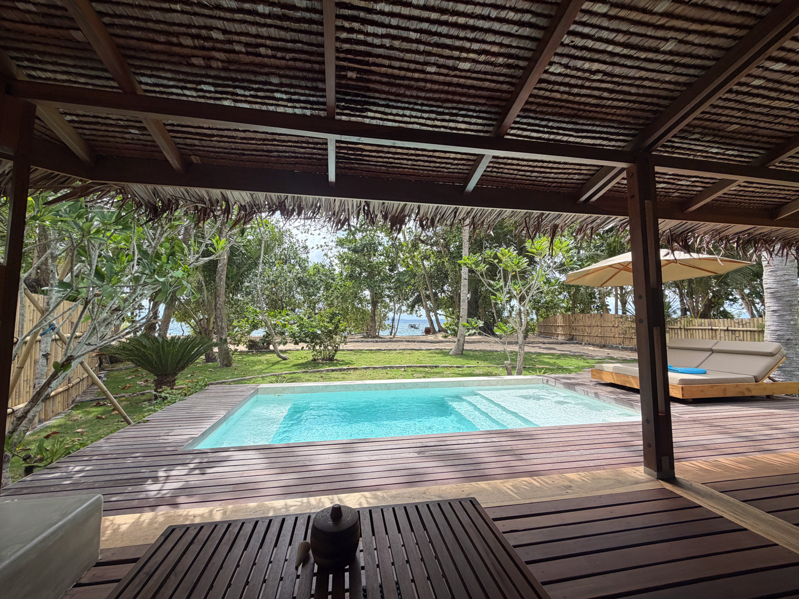 A plunge pool set into a shaded deck, the garden and the sea past the posts.