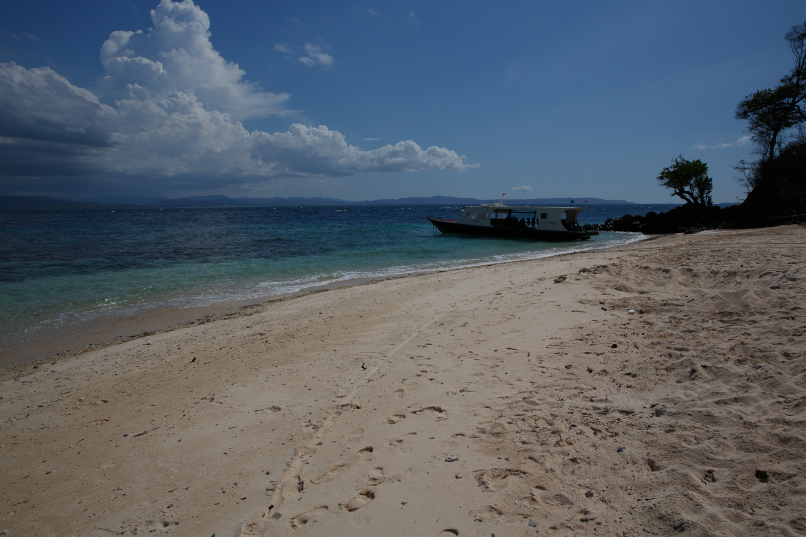 The beach curving away with a dive boat lying off the point and cloud building over the mainland.