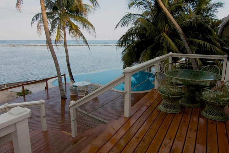 A timber deck under coconut palms, a swimming pool and the flats beyond it