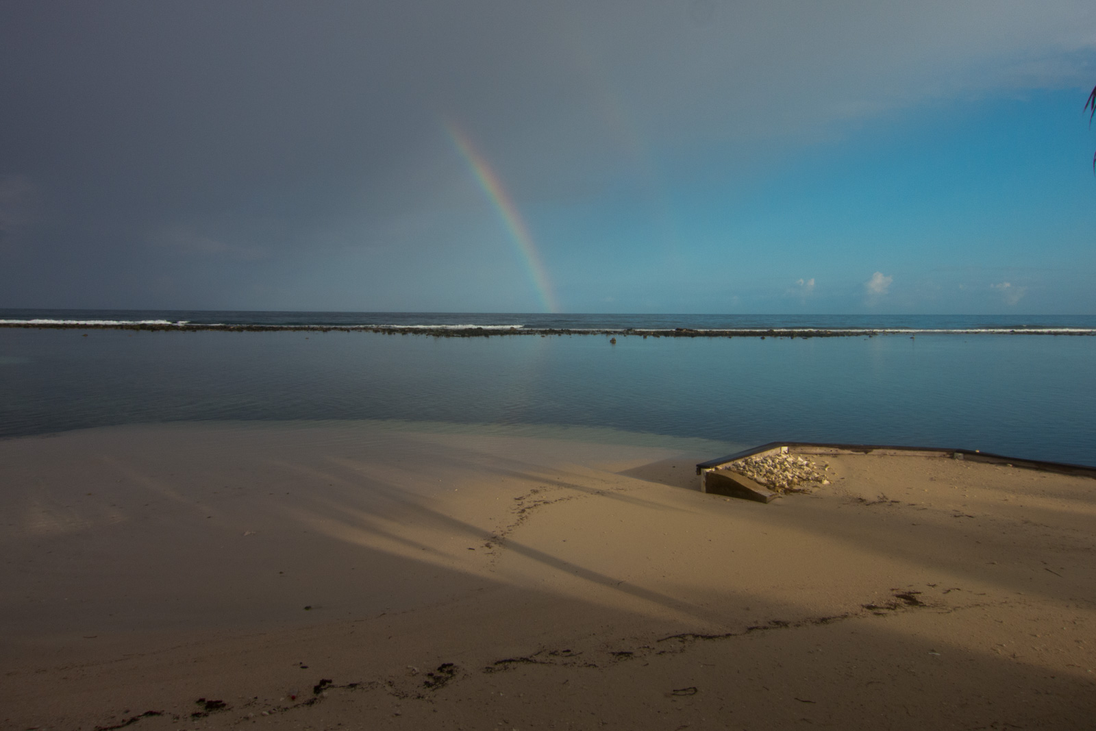 A rainbow standing over the flats under heavy cloud, the beach empty in the foreground.