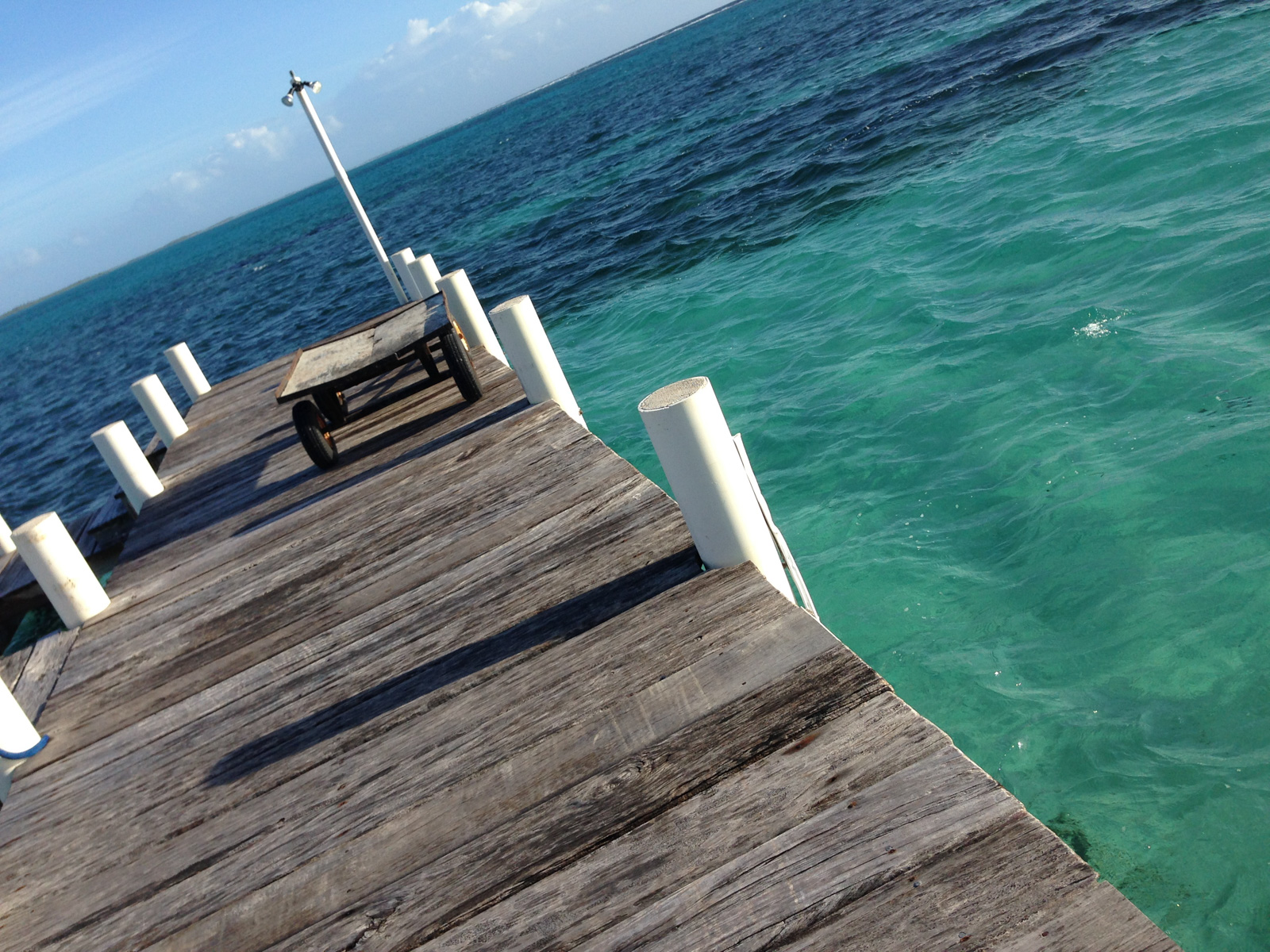 A timber dock running out over water that goes from green to deep blue at the drop.