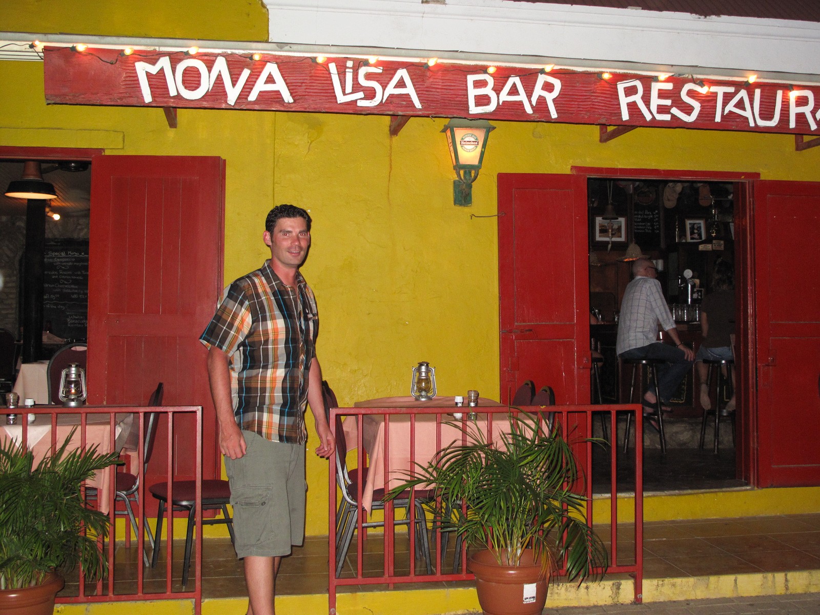 A man standing outside a bright yellow and red painted bar and restaurant on a Bonaire street