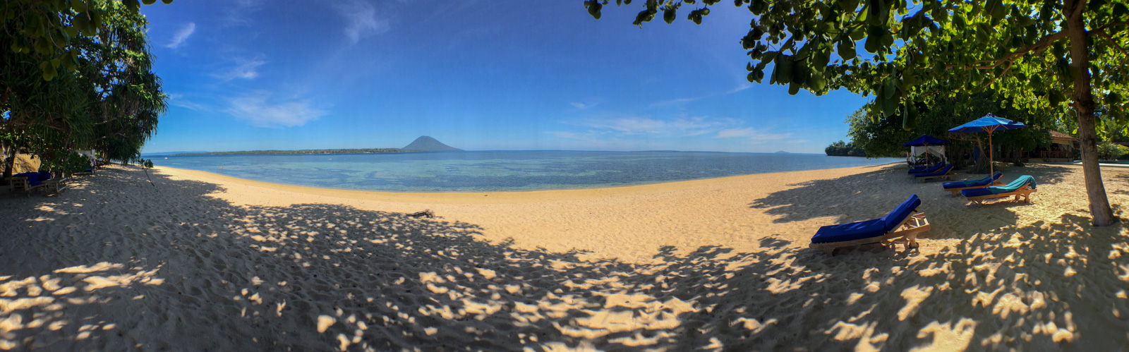 The beach looking north, an island standing offshore and loungers set back under the trees.