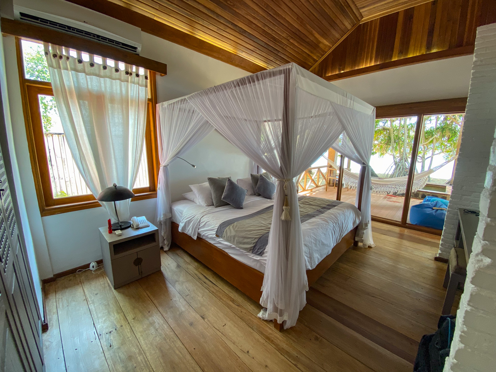 A canopied bed in a room panelled and ceilinged in timber, windows on both sides open to the garden.