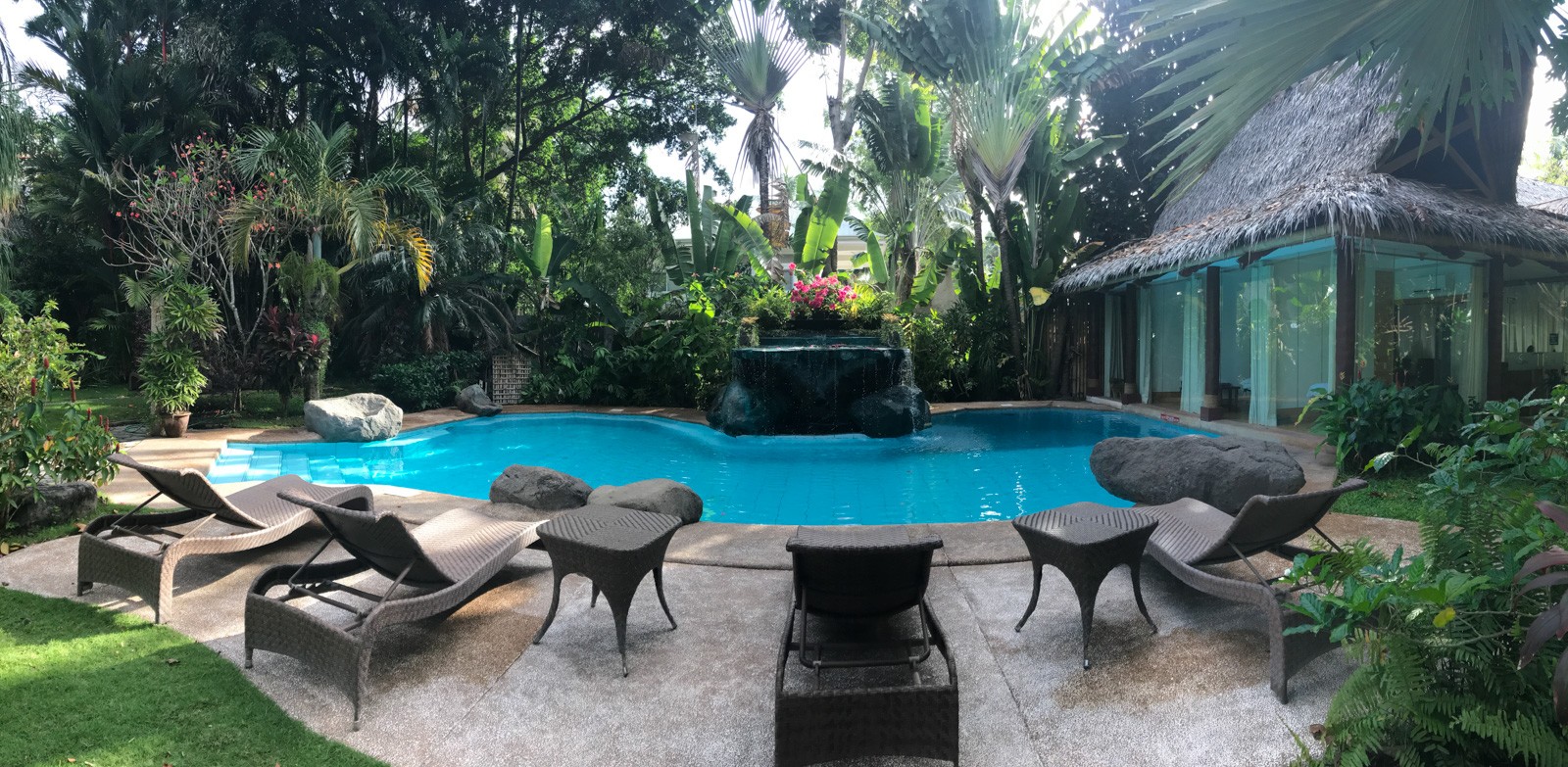A swimming pool with a stone water feature at one end, loungers and low tables set around it