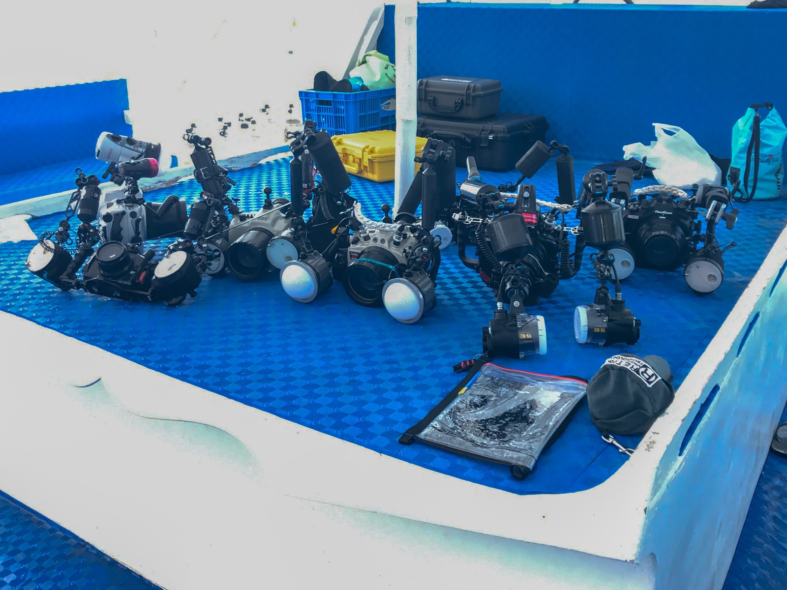 Underwater camera housings with strobes and arms laid out in rows on a blue-topped bench in a camera room
