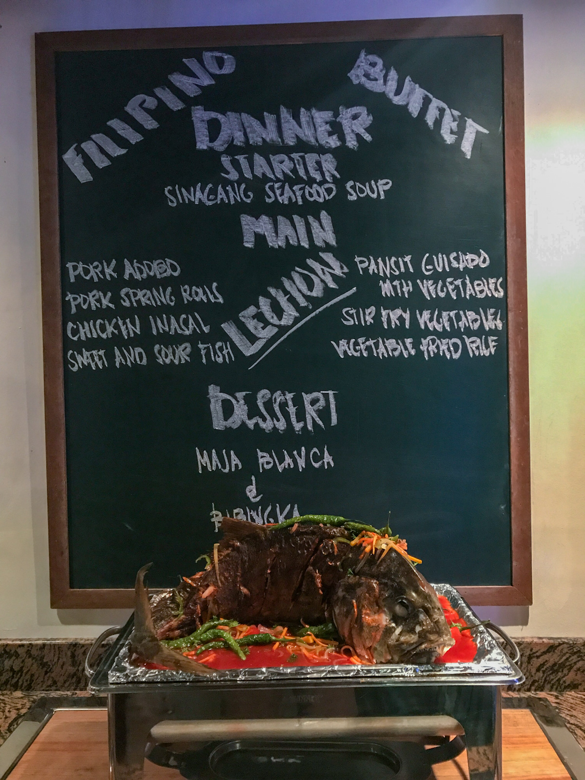 The evening's buffet menu chalked on a blackboard, the roast standing in its dish on the counter below.