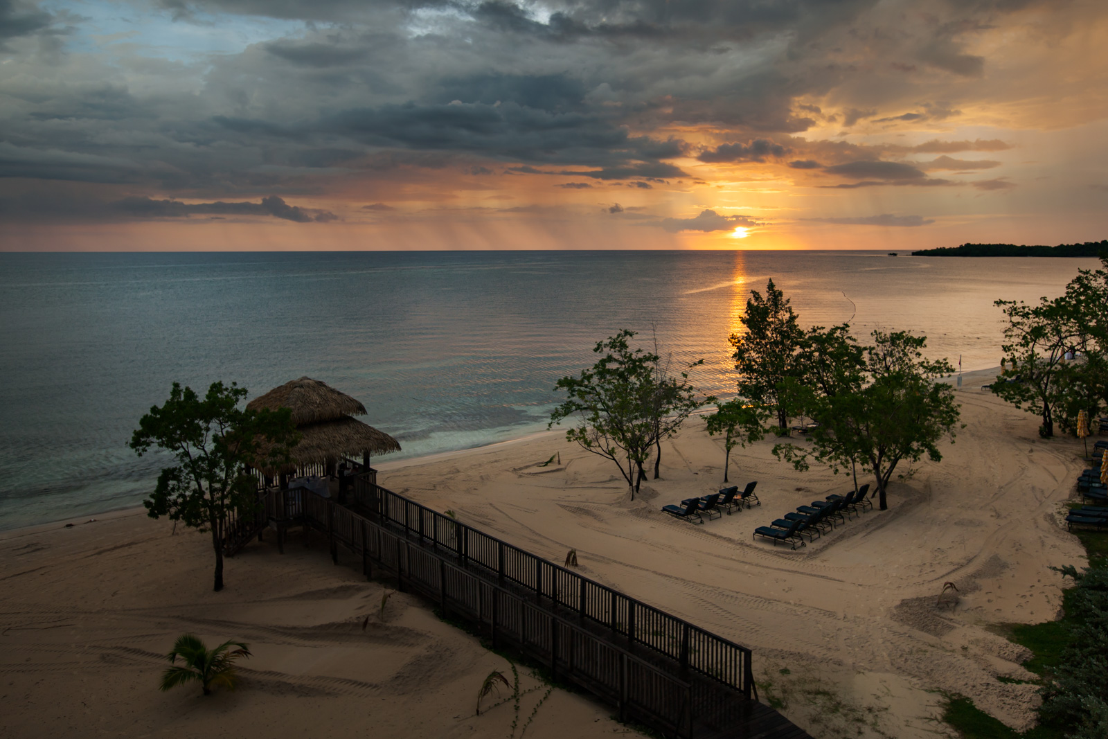 Sunset down the length of Seven Mile Beach, loungers and a thatched shelter on the empty sand.