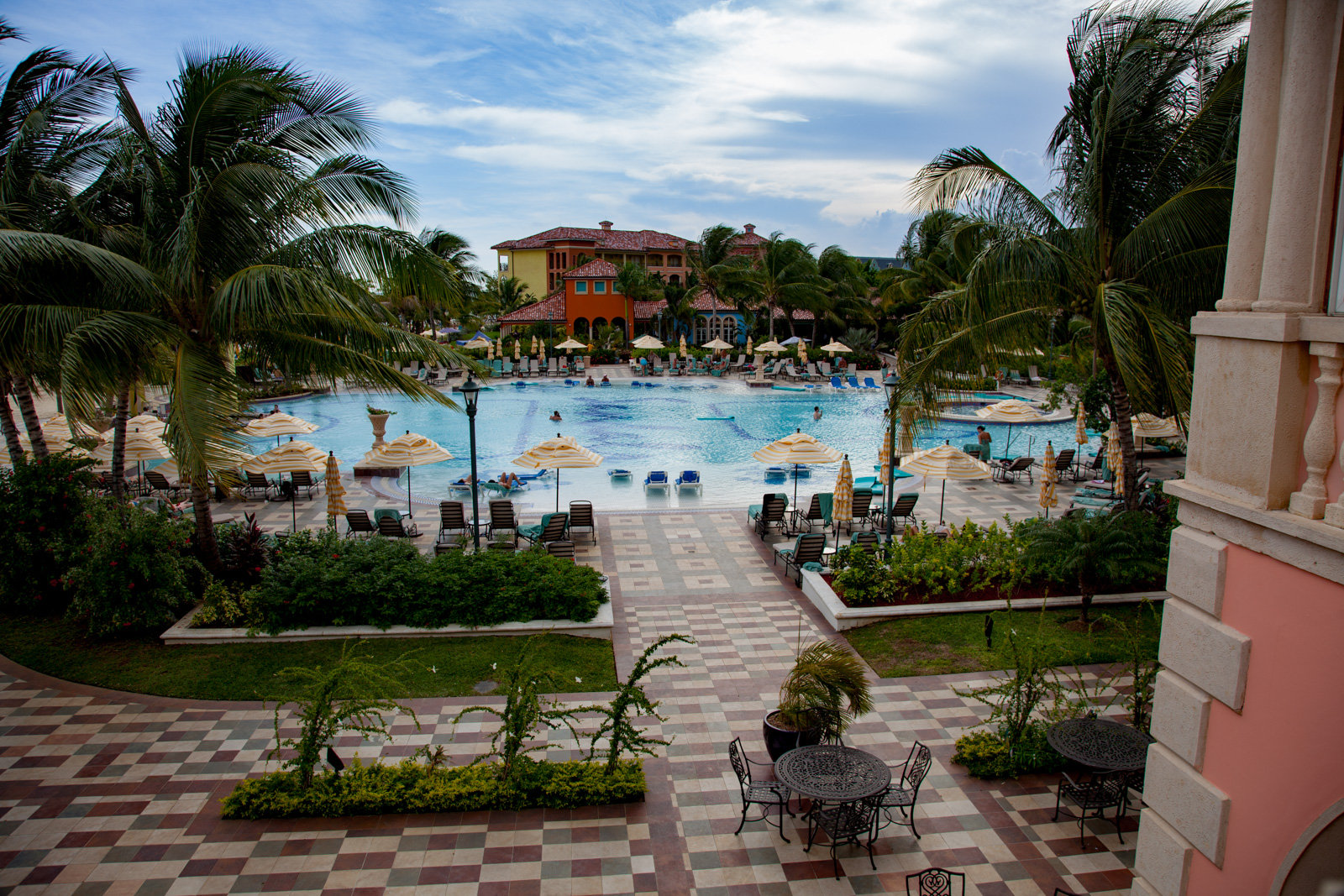 The main pool from the terrace, parasols and loungers round it and the resort buildings behind the palms.