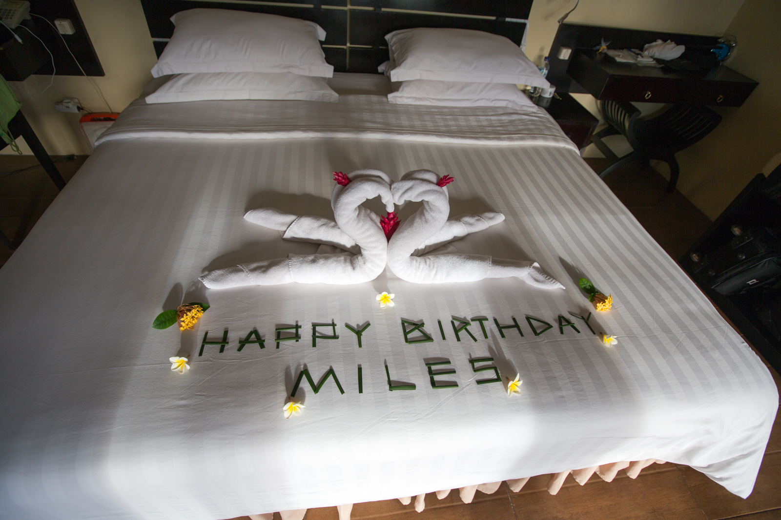 A bed turned down with towels folded into two swans and a birthday message spelled out in frangipani heads.