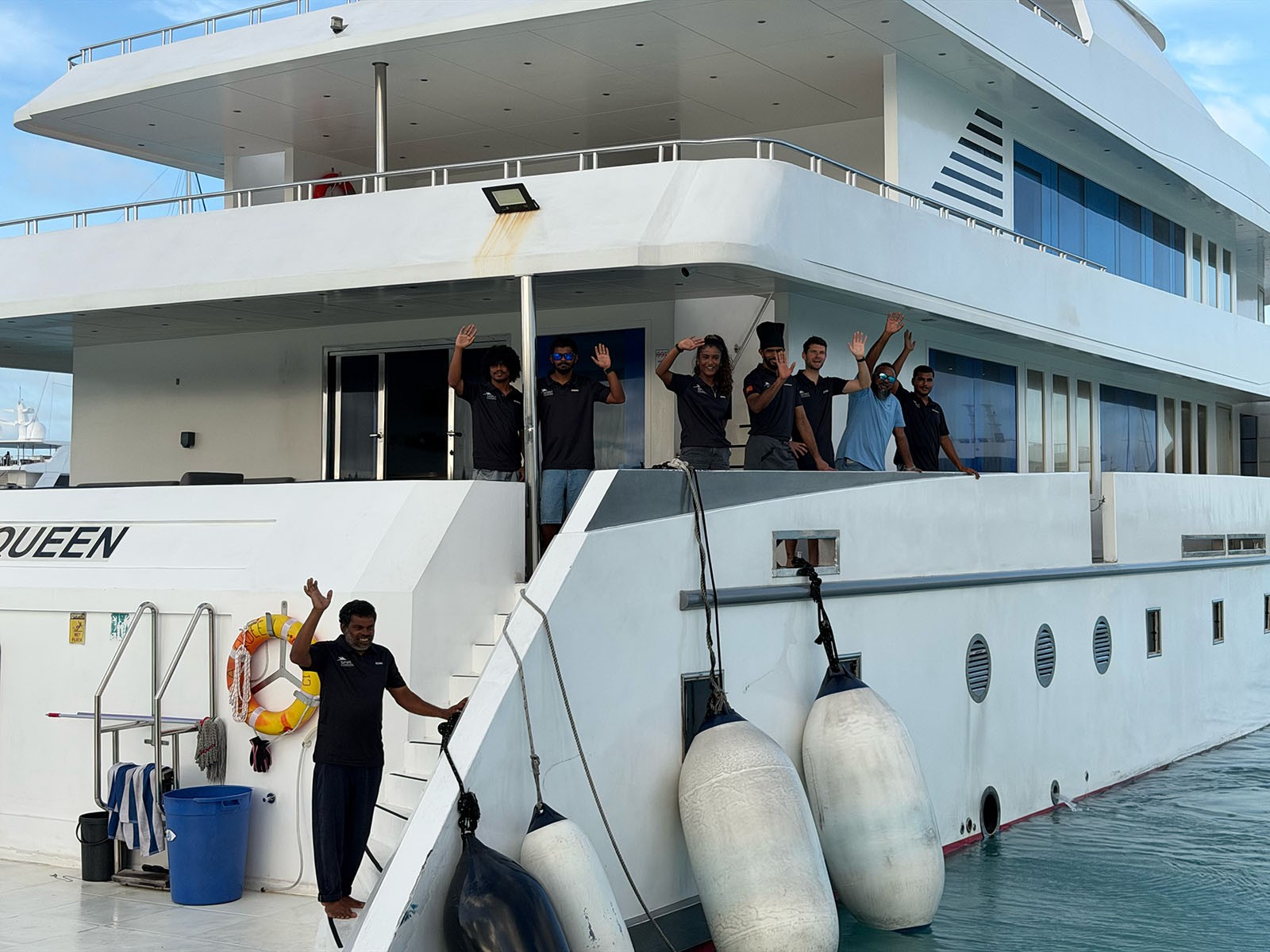 Crew and guests lining the rail of a white liveaboard, the name Aqua Queen on the hull below them