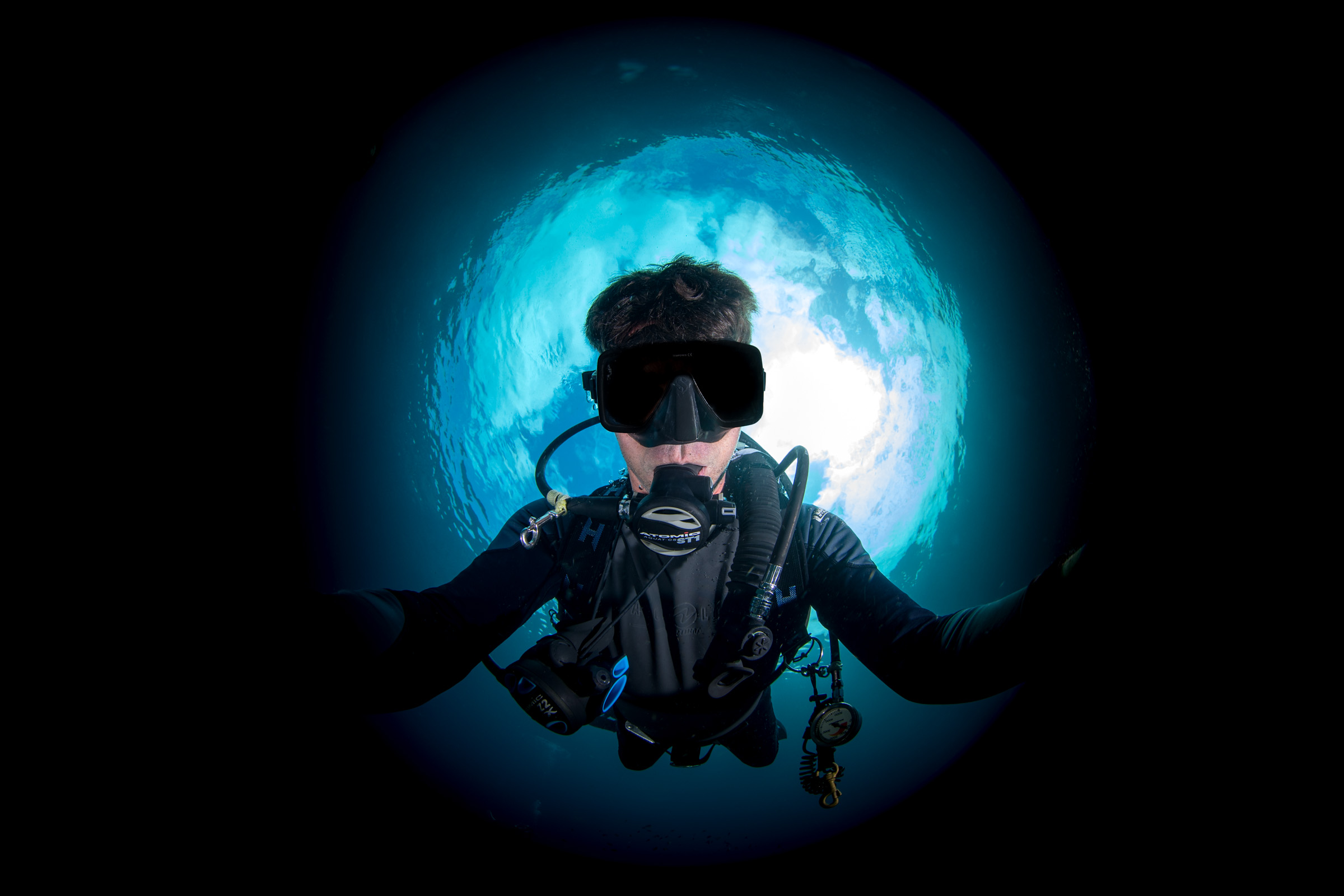Miles Nurse, fisheye self-portrait underwater, mask and camera dome to the lens, the sunball behind him