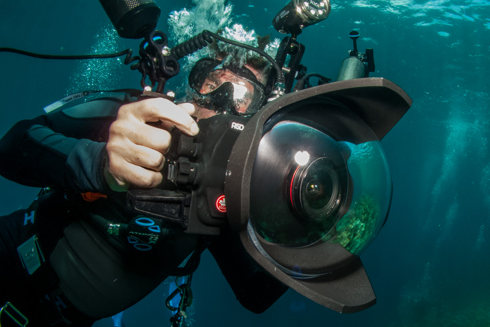 Miles close to the lens, hand on the housing behind a wide dome port, green water and a video light above him