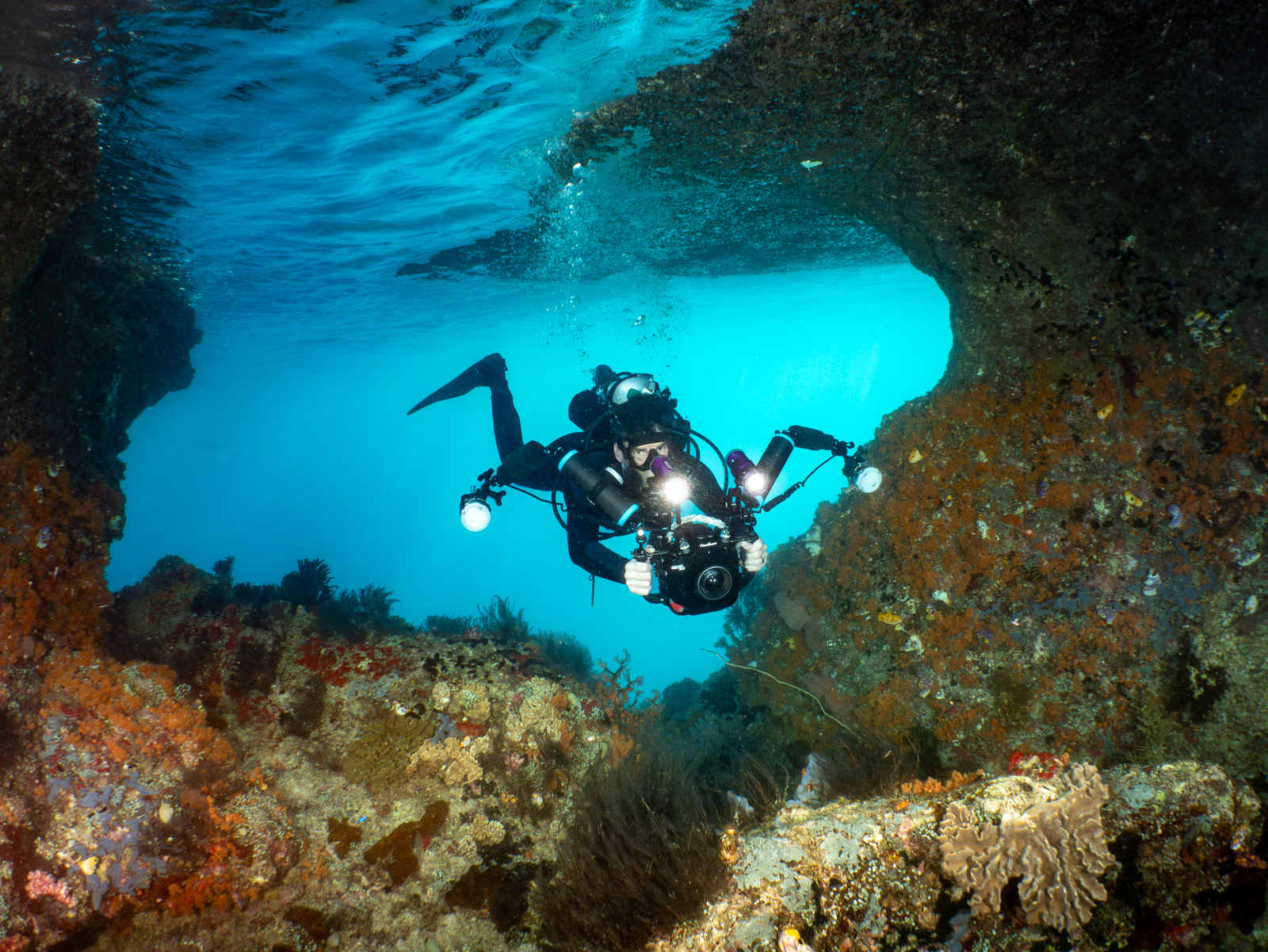 Miles Nurse with camera and twin video lights, framed in a coral swim-through, Raja Ampat