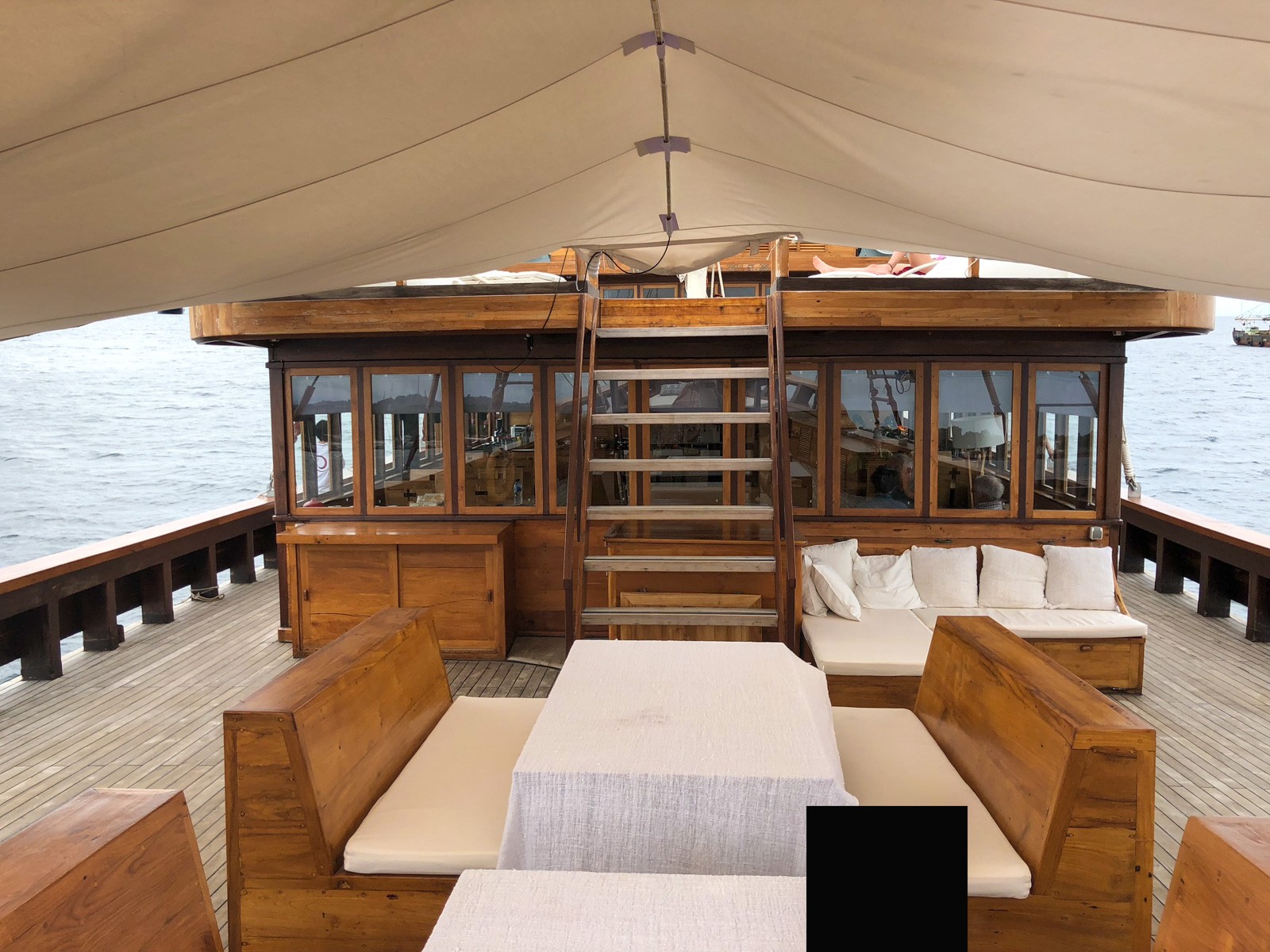 The saloon of a wooden liveaboard, benches and cushions built into the timber under a canvas roof