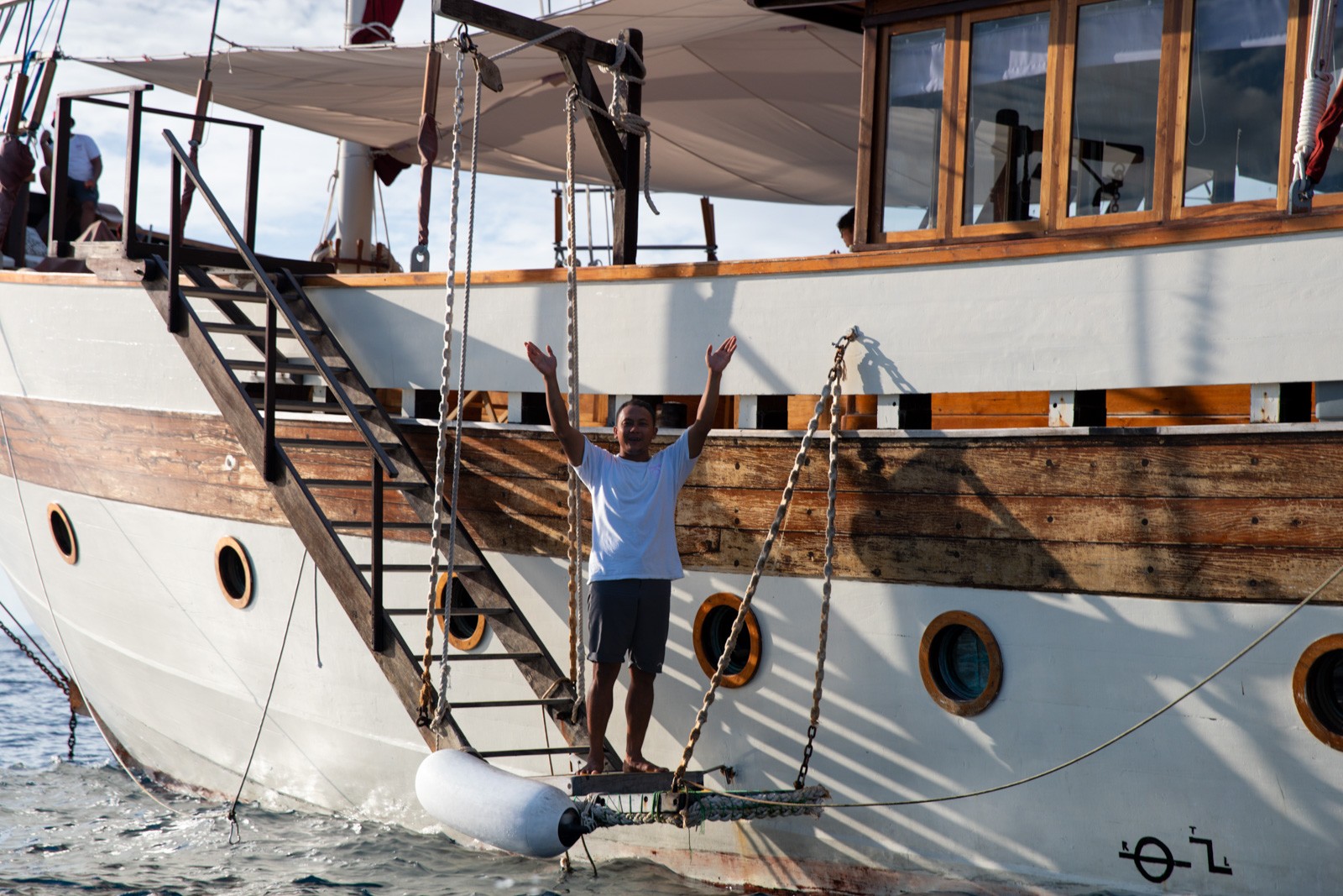A crew member on the hull of a phinisi, working from the boarding ladder above the waterline