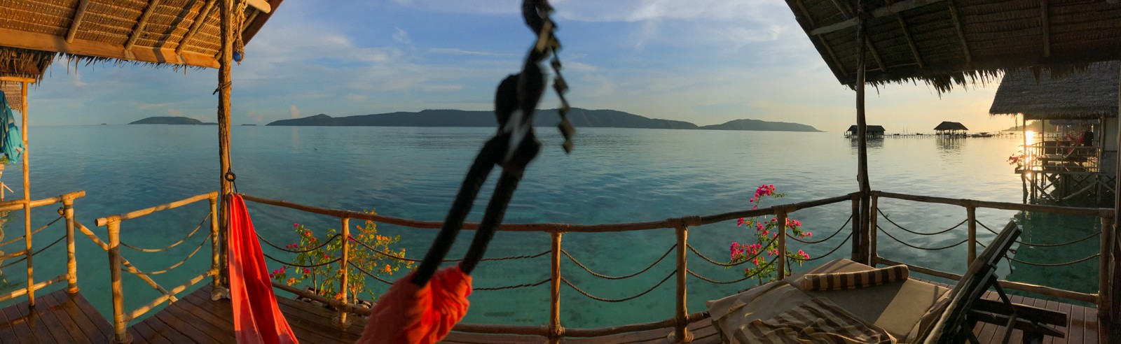 A shaded deck over the water, a hammock slung across it and the bay beyond