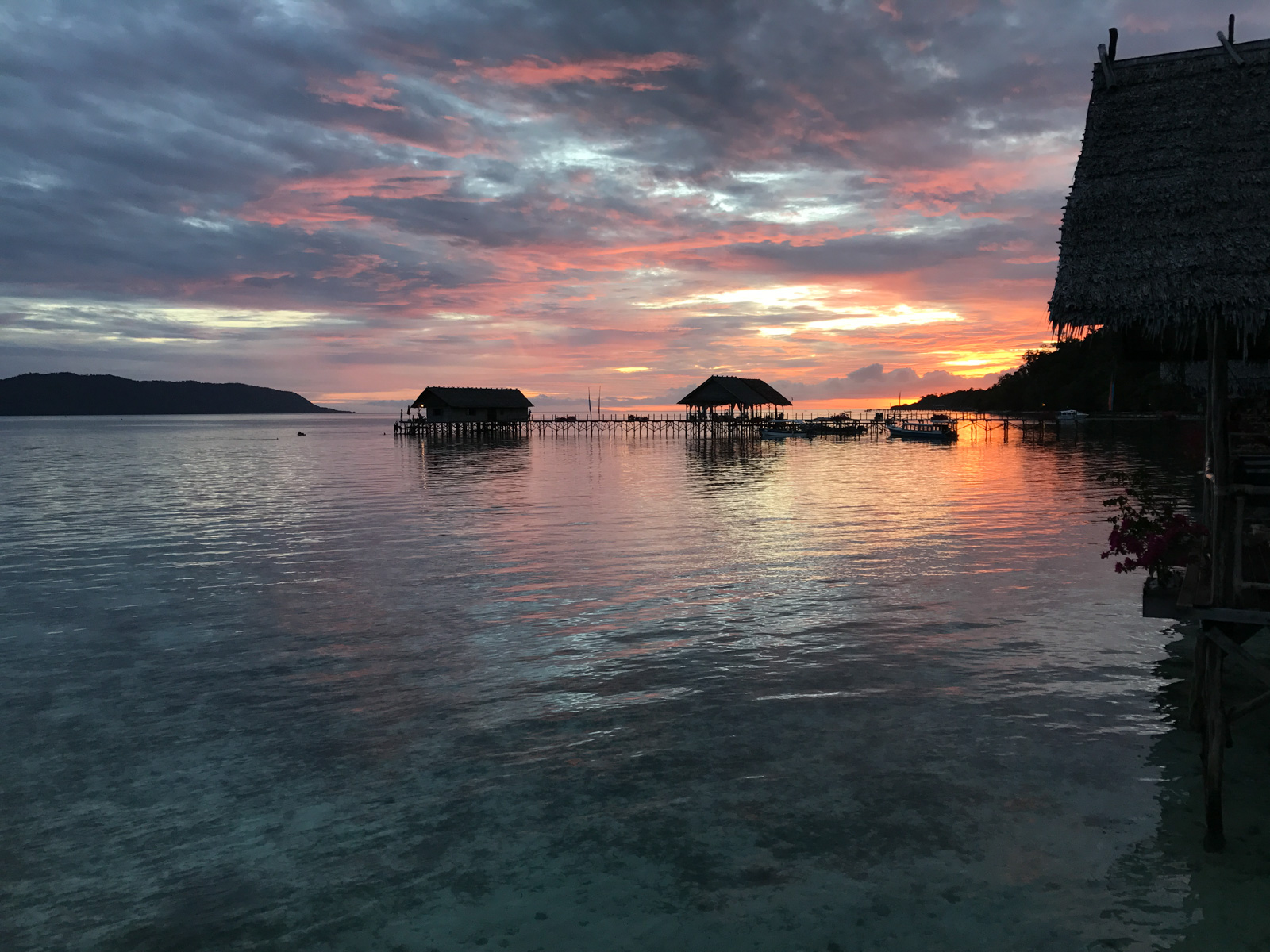 Sunset over the house reef, the overwater bungalows and the jetty strung out in silhouette along the shallows.