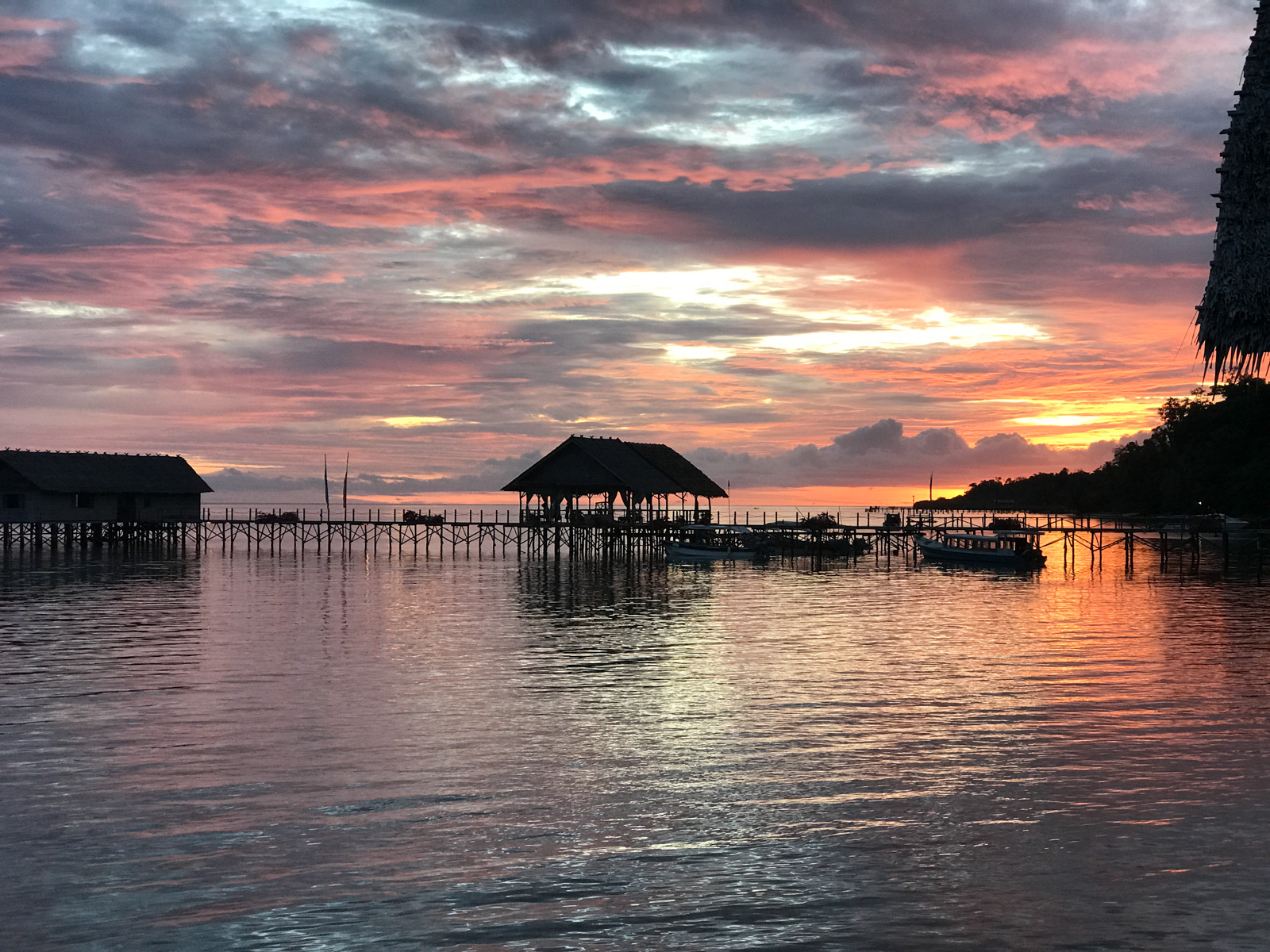 The dive jetty and its thatched shelter against a red sky, boats tied along the far end.