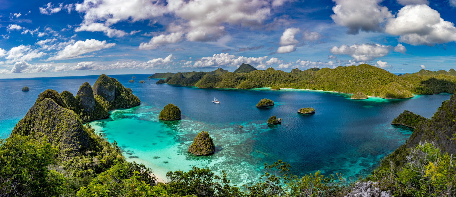 Karst islets scattered across turquoise shallows, seen from high ground under a sky full of cumulus.